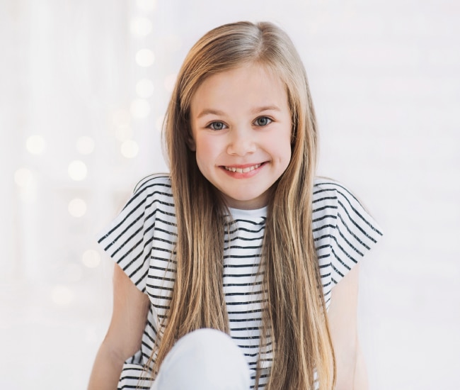Young girl smiling at camera wearing striped shirt, professional portrait against white background.