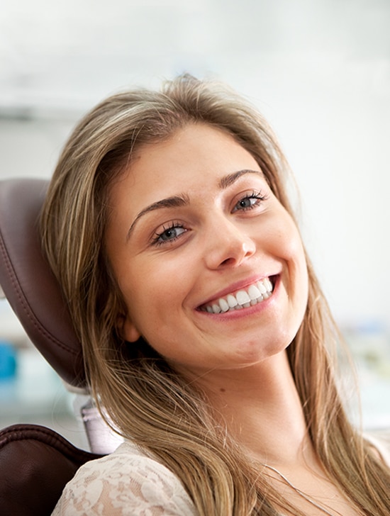 Smiling woman in dental office setting, wearing dark clothing, professional portrait.