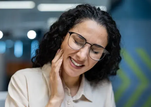 Woman with glasses touching her cheek, smiling in a dental office setting.